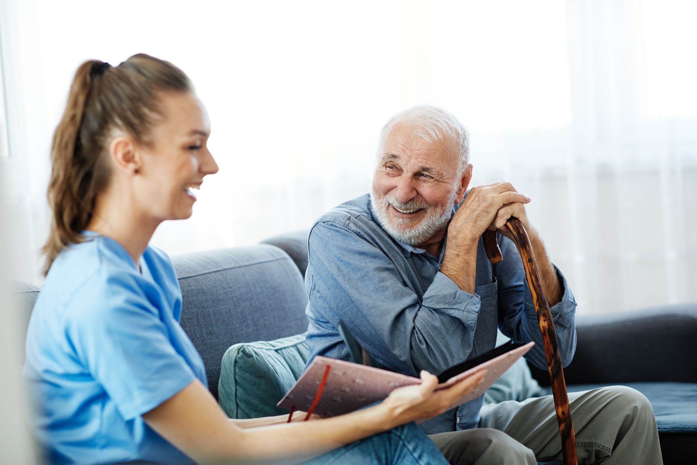 Senior man with a cane looking at a photo album with his caregiver